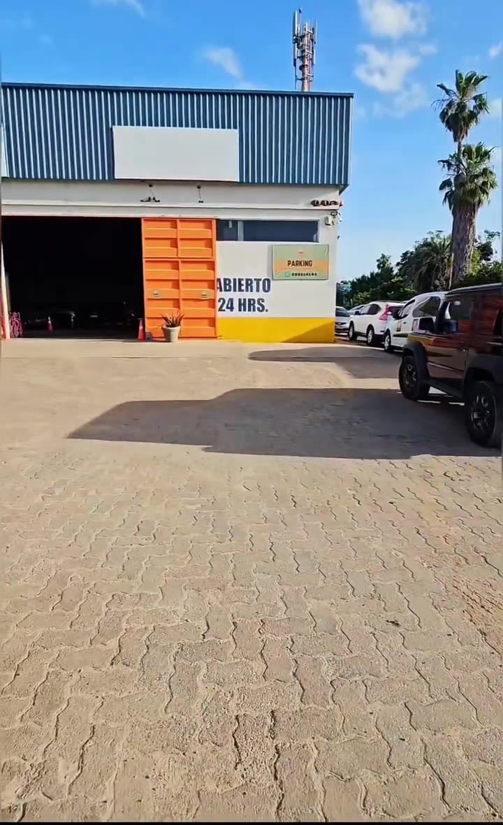 Frente del parking: galpón blanco con portones naranjas y el cartel Abierto 24 horas